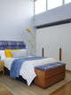 Minimalist bedroom with tall ceilings, featuring Breakwater Indigo fabric by Christopher Farr on the headboard. Geometric pattern adds bold contrast in a contemporary setting by Arent & Pyke.